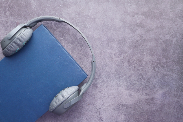 Un livre avec une couverture bleue porte une paire d’écouteurs gris.