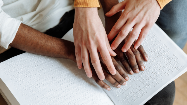 Une paire de mains guide une autre paire de mains en train de lire un livre en braille.