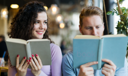 A woman holding a book smiles at the man beside her who is also holding a book.