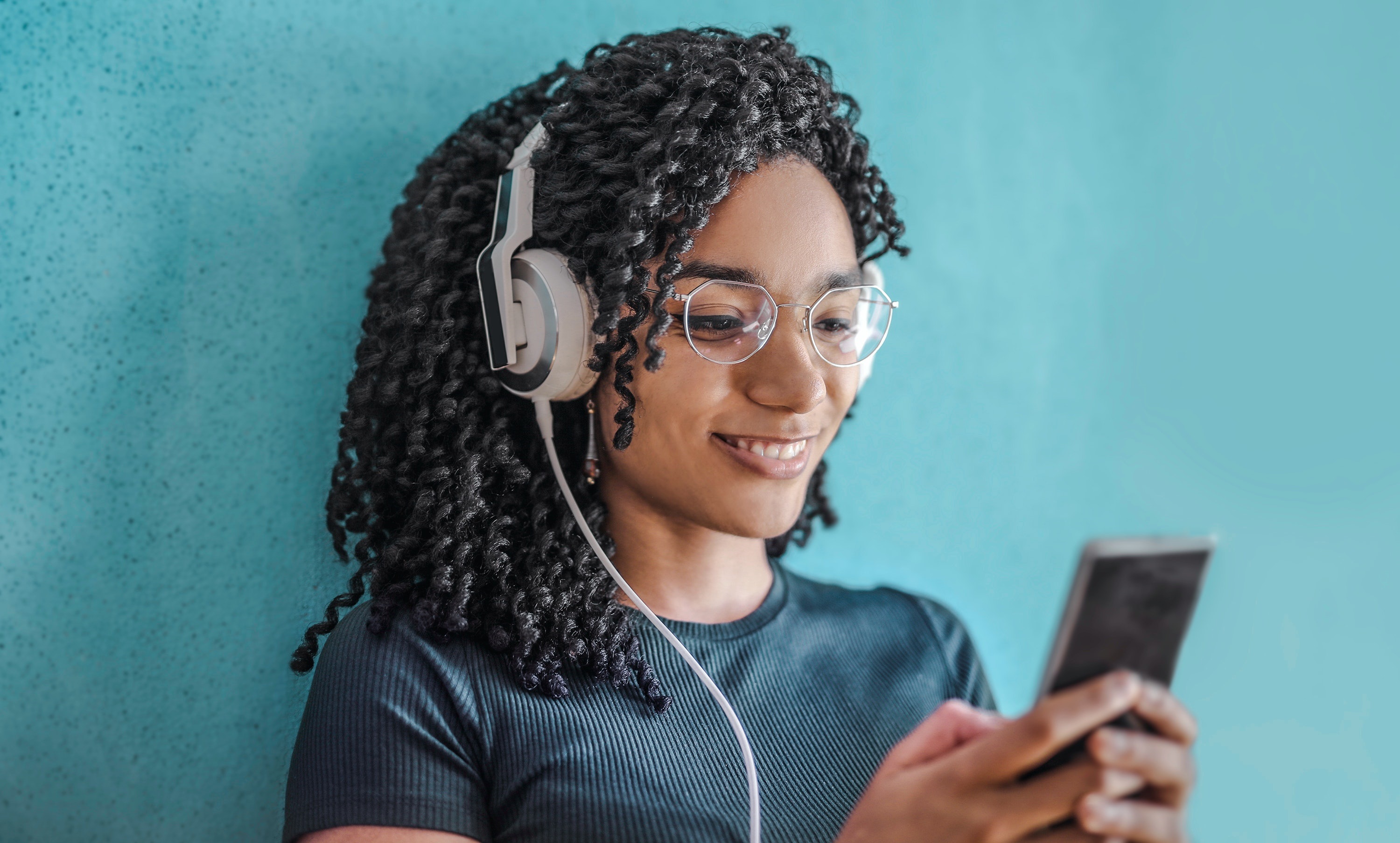 Une jeune femme noire écoutant un livre audio sur son smartphone et souriant