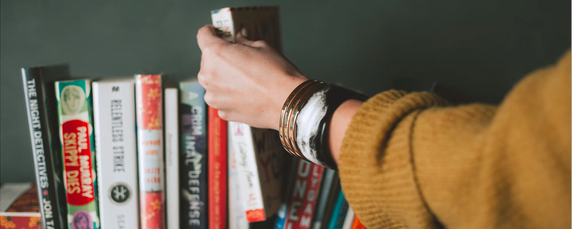 Une femme portant un pull en or et un bracelet en argent en sélectionnant un livre dans une étagère