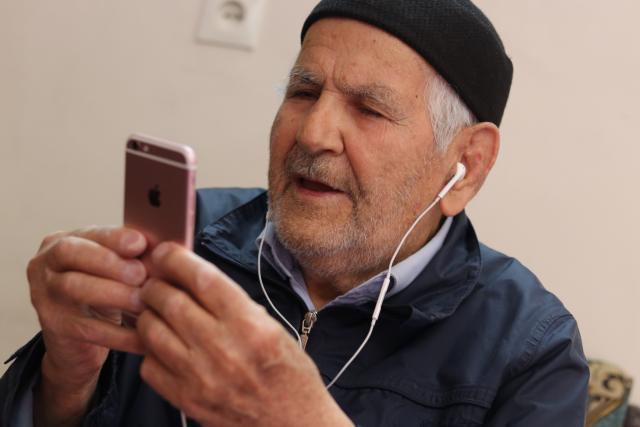 Un homme âgé dans un bonnet en tricot à l'écoute d'un livre sur un iphone