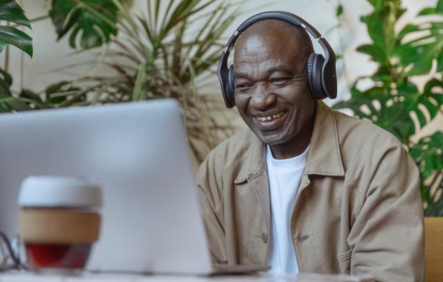 Homme noir avec des écouteurs regardant la vidéo sur l'ordinateur portable et souriant